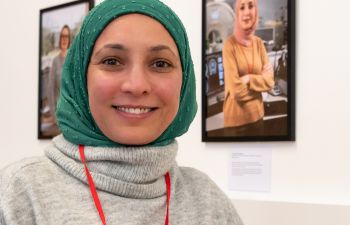 A СƵ colleague wearing a green headscarf in front of her picture which is part of the exhibition at the Library