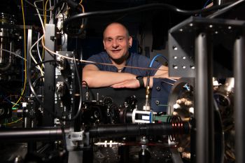 Professor Winfried Hensinger crossing his arms behind a prototype of a quantum computer in the quantum technologies lab at the СƵ